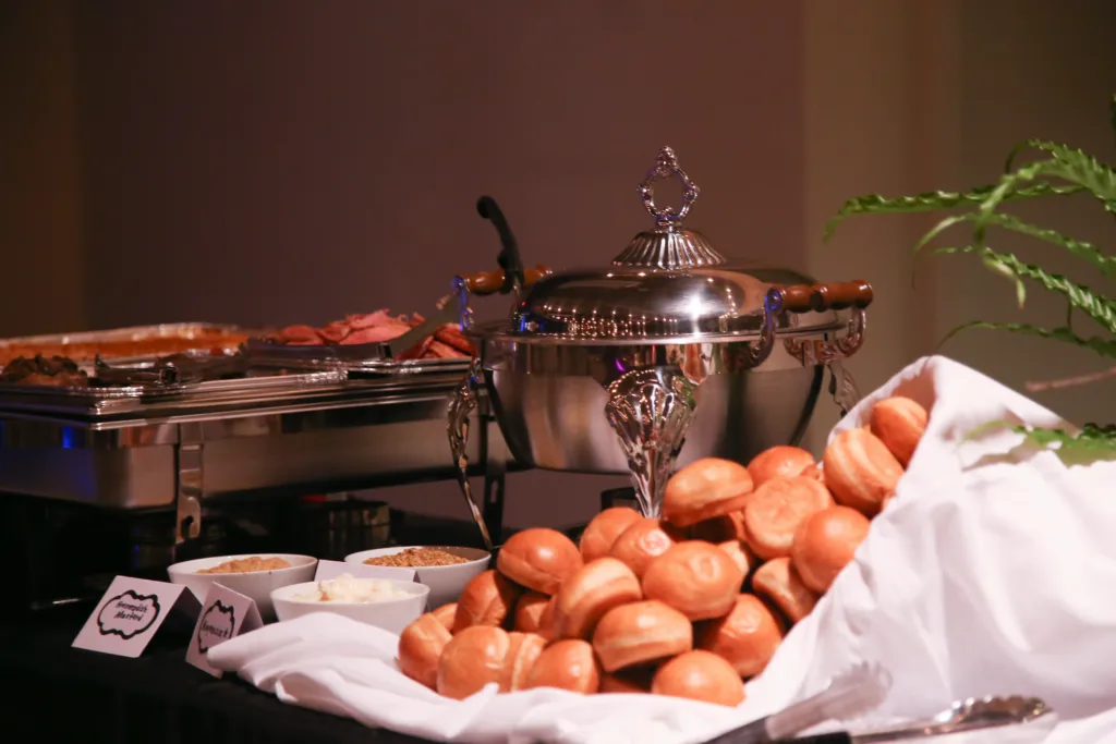 A catered buffet at the McKissick Center with chafing dishes, condiments, and a basket of fresh rolls.